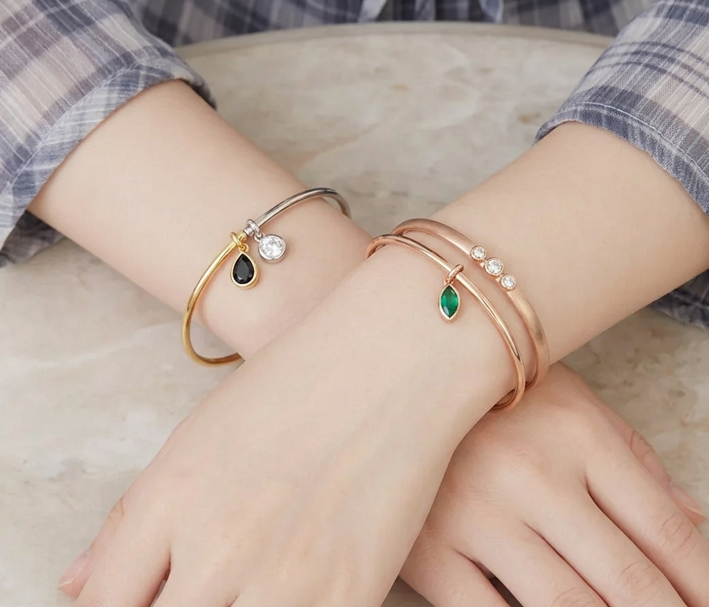 A close-up shot of two hands crossed on a grey marble-textured surface, wearing bangles.
